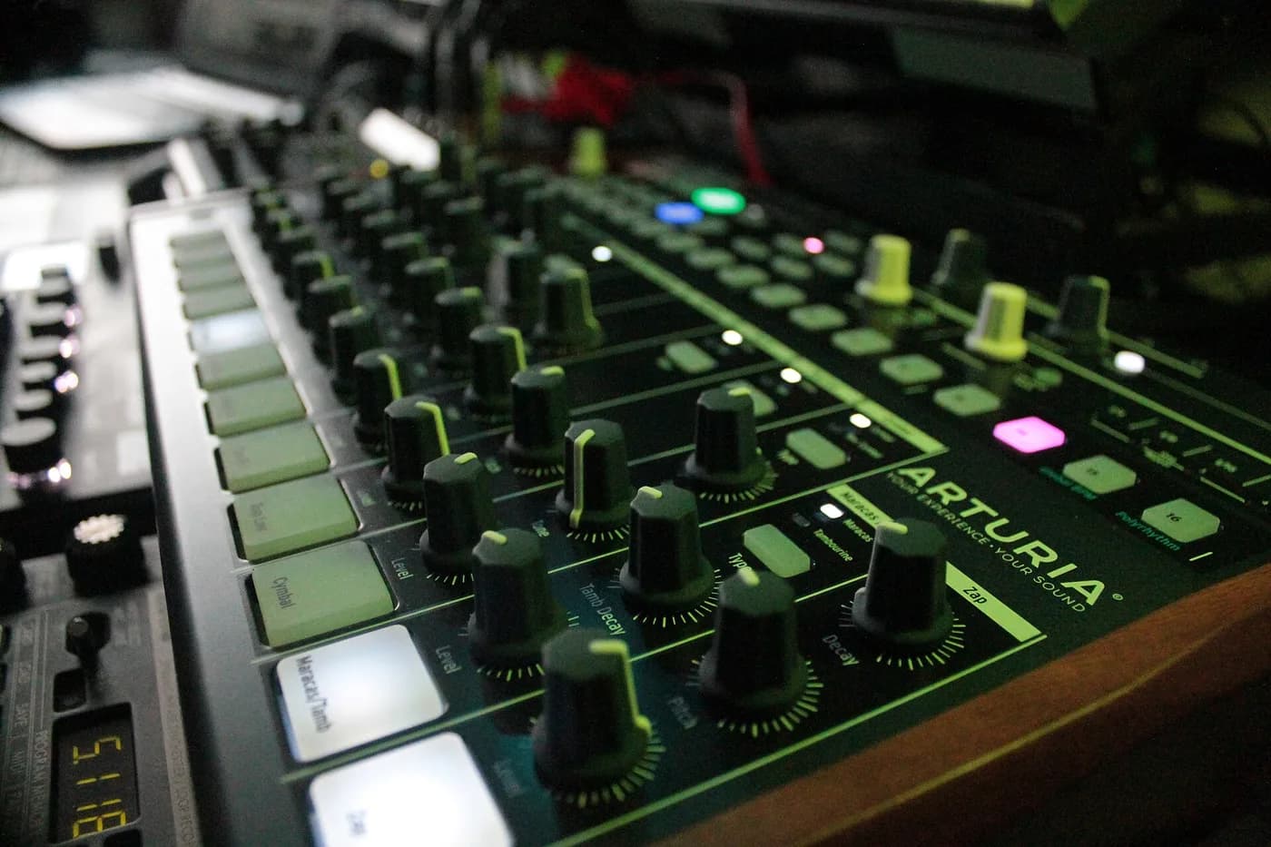Close-up of an Arturia DrumBrute at an angle, showing rows of pitch, decay and level knobs lit by green panel markings.