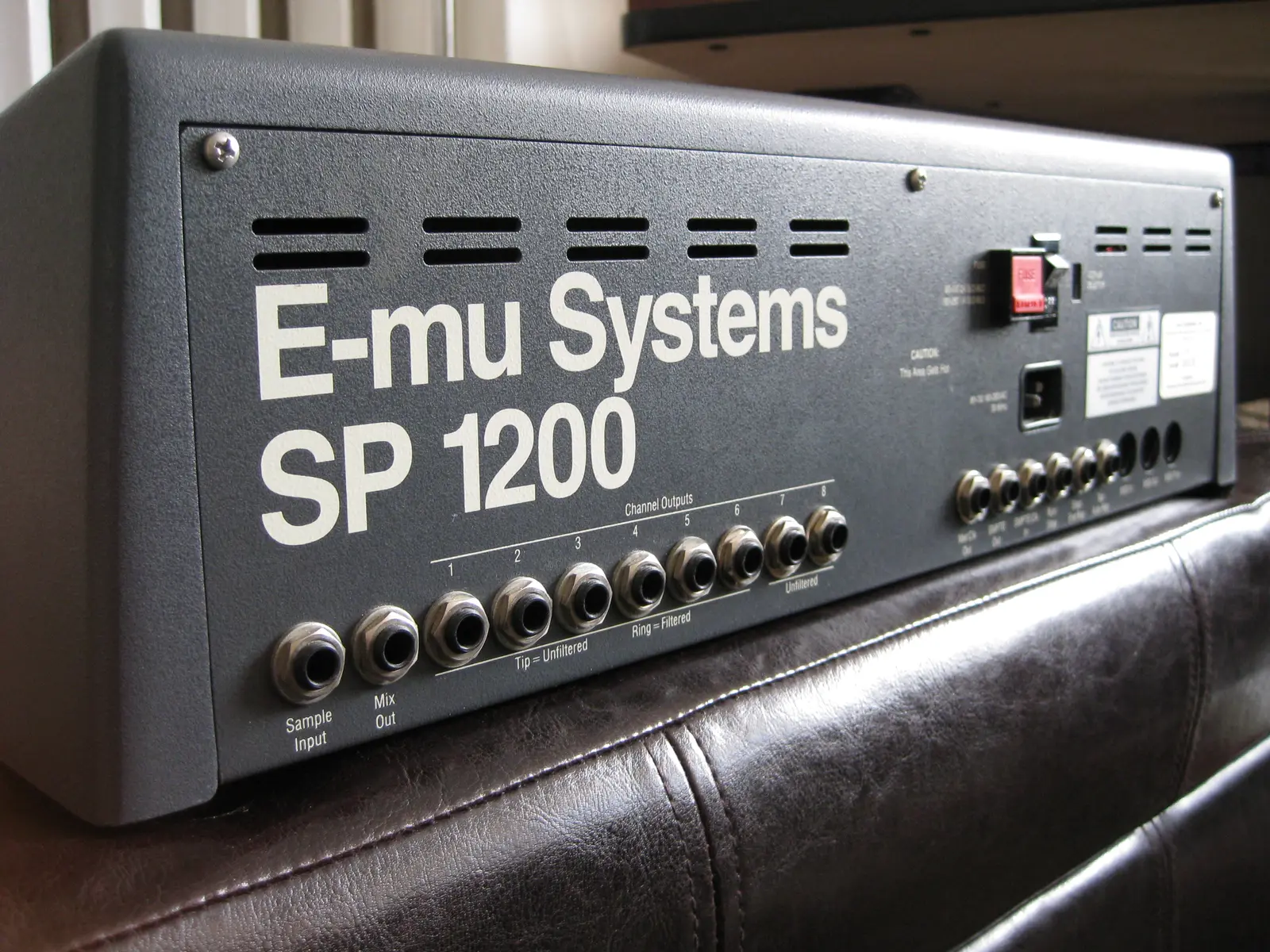 Rear panel of an E-mu SP-1200 showing the sample input, the mix output and eight channel outputs. Printed labels read “Tip = Unfiltered, Ring = Filtered” under outputs 1 to 6 and “Unfiltered” under outputs 7 and 8.