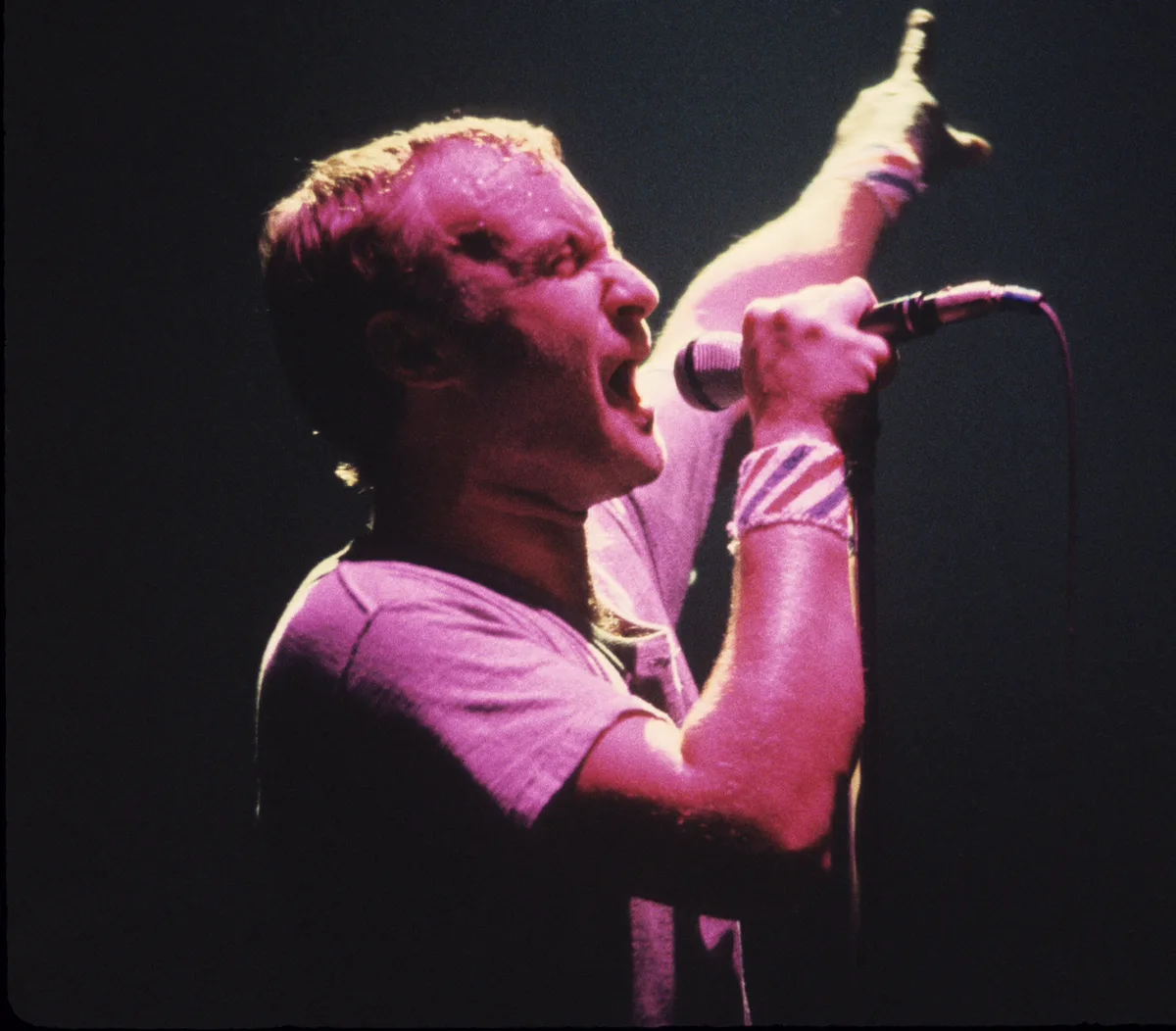 A singer performing live at a microphone stand under magenta stage lighting.