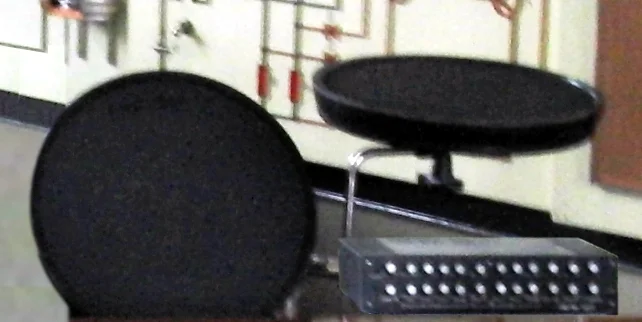 A Lel UDS percussion synthesizer: a small metal box with a row of knobs, played from two round rubber drum pads mounted on stands.