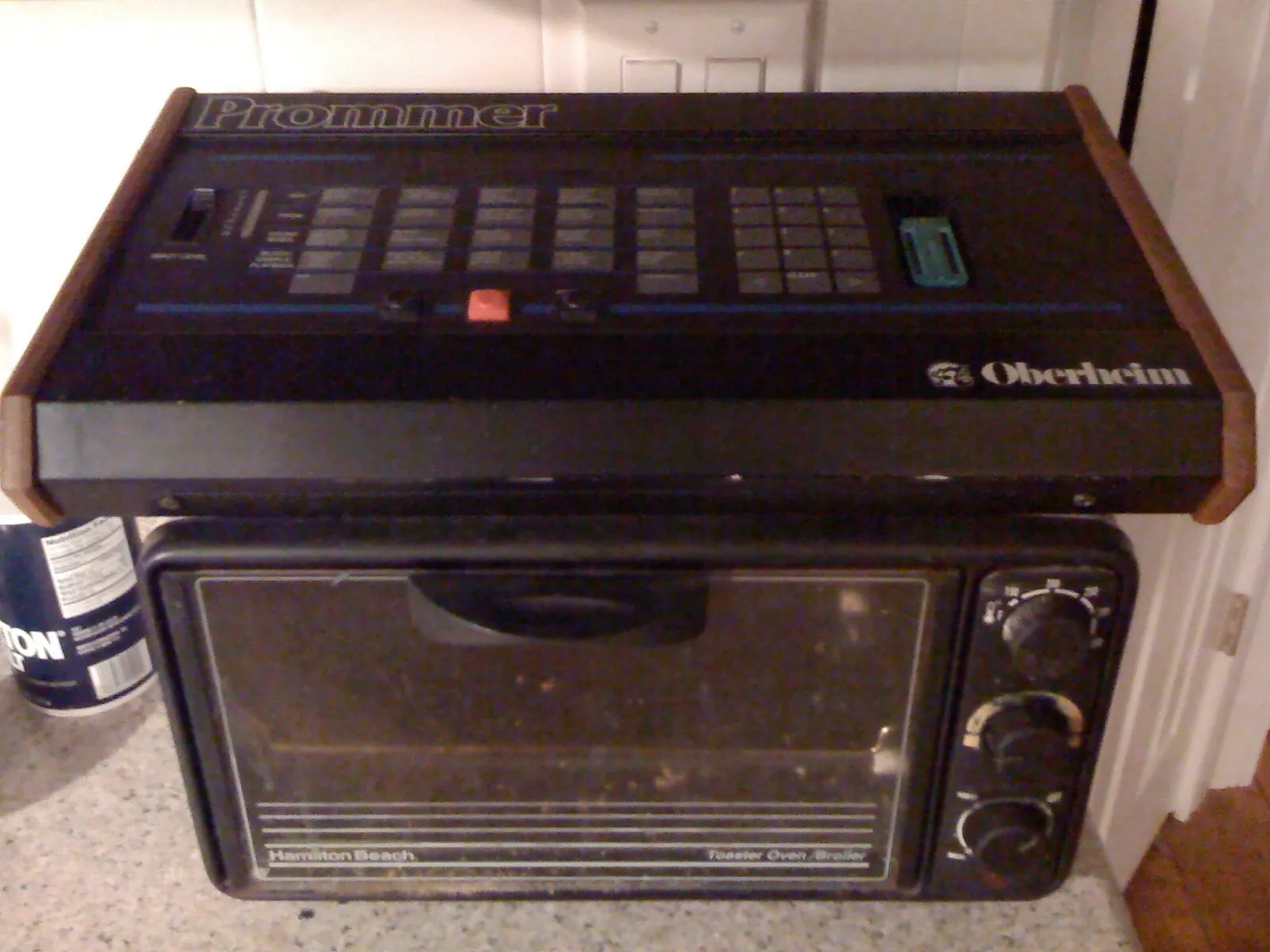 An Oberheim Prommer in the same black and wood styling as the DMX, with an input level slider, rows of function buttons and a green chip socket on the right where a blank EPROM is inserted to be written.
