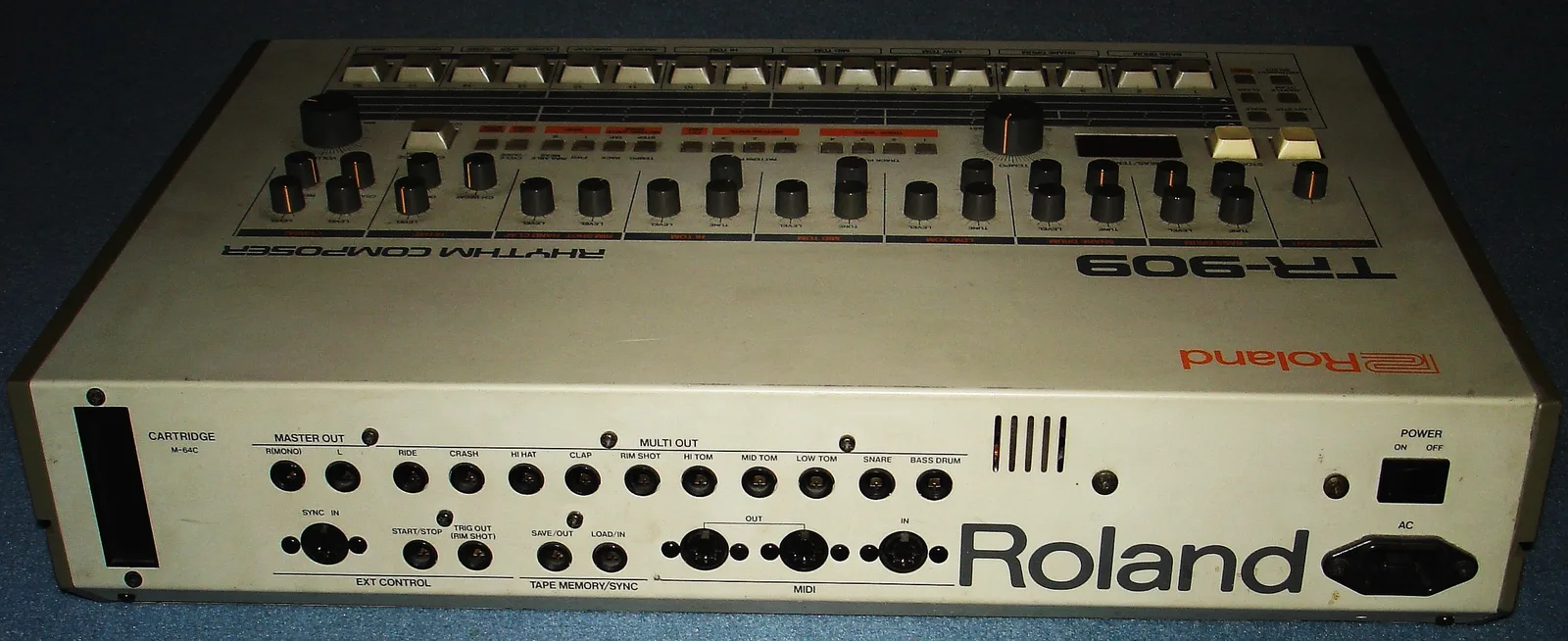 Rear panel of a TR-909: the M-64C cartridge slot, master out, ten multi out jacks from ride to bass drum, the DIN sync input, start/stop and rim shot trigger jacks, tape save and load jacks, and MIDI in and two MIDI outs.