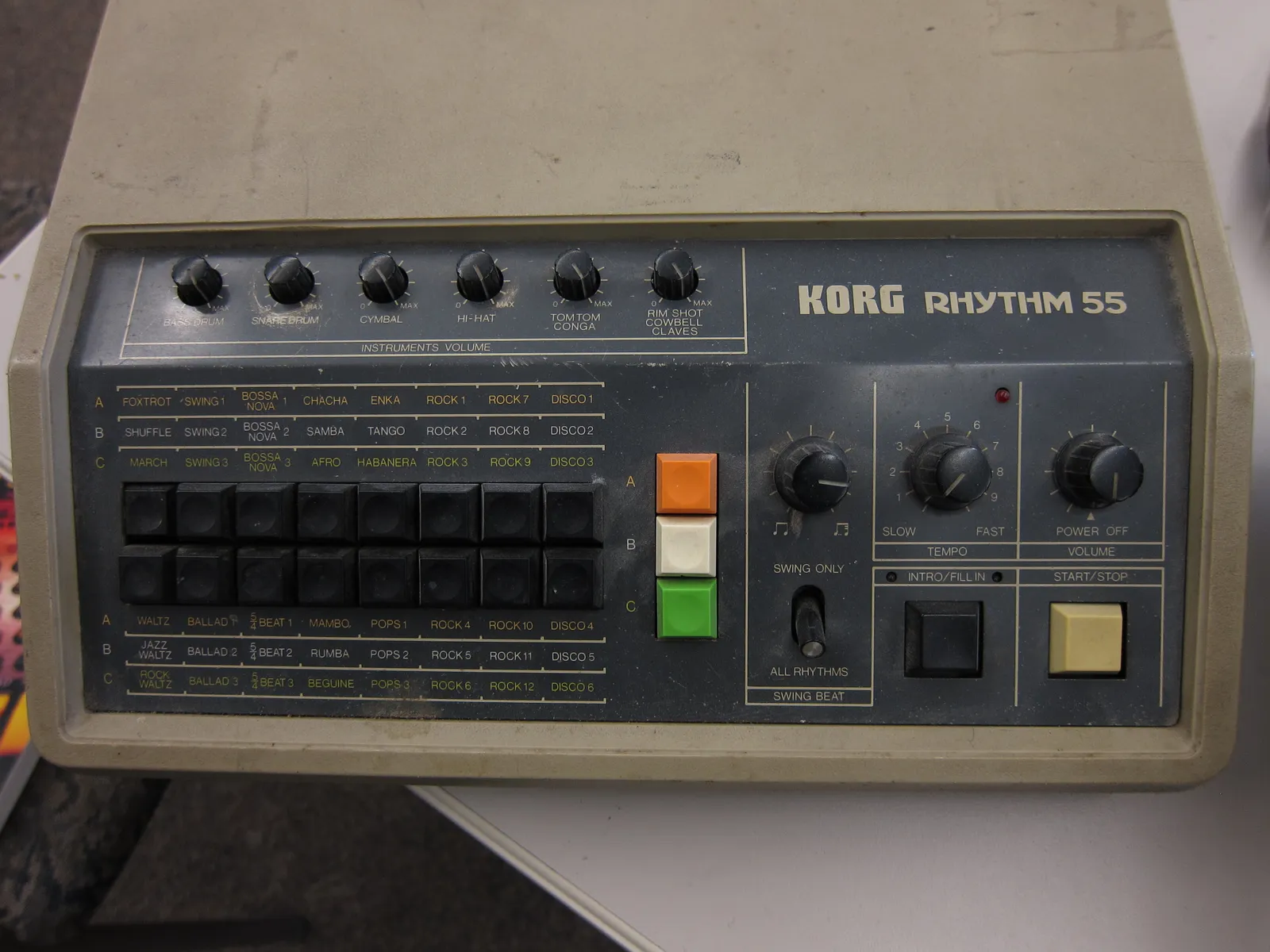 A Korg Rhythm 55 (KR-55) with six instrument volume knobs across the top, sixteen rhythm buttons labelled in three banks A, B and C, and intro/fill-in and start/stop buttons on the right.